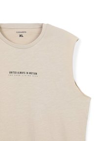 Maglietta beige senza maniche realizzata in un tessuto morbido e leggero. Presenta un collo rotondo e una stampa con la scritta: "UNITED ALWAYS IN MOTION" in un colore scuro.