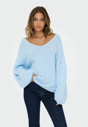 lichtblauwe gebreide trui met een wijde V-hals, oversized mouwen en geribde manchetten, gecombineerd met donkere skinny jeans. Zachte textuur en ontspannen pasvorm.