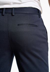 Pantalons ajustés bleu marine avec une texture lisse, présentant des passants de ceinture, une poche latérale discrète et une coupe épurée.