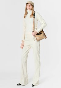 Mono crema de cuello alto con cuerpo ceñido y piernas acampanadas. Combinado con un bolso de hombro marrón claro. Zapatos negros de punta afilada.