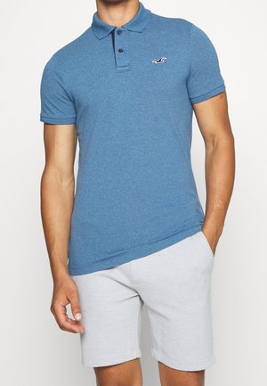 Blue polo shirt made of textured fabric, featuring a three-button placket, short sleeves, and a small logo on the chest.