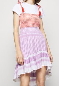 Colorful dress featuring a red patterned bodice, white T-shirt sleeves, and a lavender skirt with layered textures and fringed hem.