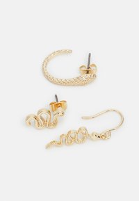 Brincos de ouro com três designs: um aro em forma de serpente, um estilo ondulado fluido e um padrão de serpente detalhado; textura suave.