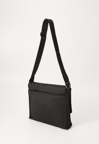 Sac à bandoulière noir en synthétique avec sangle réglable, compartiment principal zippé et poche avant plate. Texture lisse, forme rectangulaire.