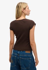 Top corto de manga corta marrón con textura acanalada, con un escote festoneado y dobladillo sin terminar, combinado con jeans de mezclilla azul de cintura alta con parche y bordado.