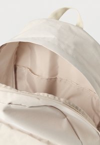 Ανοιχτό μπεζ σακίδιο με λείο, ανθεκτικό εξωτερικό. Το εσωτερικό διαθέτει απαλό επένδυση με μια μικρή τσέπη και χειρολαβή στο πάνω μέρος.