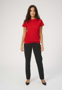 Rød kortærmet T-shirt i bomuldsmateriale, kombineret med sorte skræddersyede bukser og spidse sorte hæle; enkelt design, klassisk pasform.