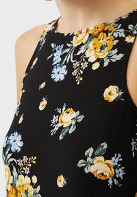 Vestido negro con flores y un escote alto. Presenta flores amarillas y azules sobre una tela texturizada. El primer plano muestra patrones intrincados.