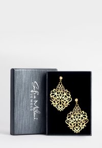 Guldfiligran hängande örhängen med intrikat blommönster, visade i en svart sammetsklädd smyckeslåda med en silverlogotyp på locket.