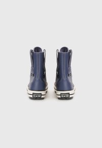 Navy blue rubber high-top boots with textile lining, Converse logo patch, pull tabs, and white rubber soles featuring black stripes.