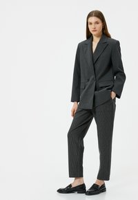 Grijze dubbelreeks blazer met notch-kraag, gecombineerd met grijze pinstripe broek en zwarte instappers. Slim fit en een soepele textuur.