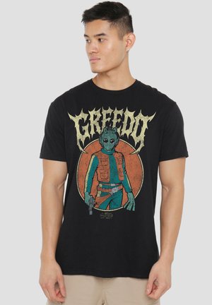 Man wearing black t-shirt with graphic of Star Wars character Greedo holding a blaster and large text "GREEDO" above.