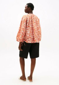 Rød- og hvidblomstret skjorte med puffede ærmer og indsamlet ryg, kombineret med sorte shorts og lyse sandaler, der viser en afslappet pasform.