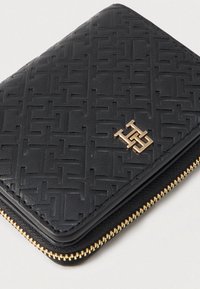 Portefeuille zippé noir texturé avec un motif géométrique. Équipé de quincaillerie dorée et d'un logo en relief à l'avant. Matériel en cuir lisse.