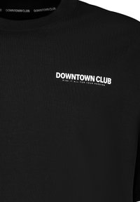 Schwarzes Baumwoll-T-Shirt mit rundem Halsausschnitt. Auf der Vorderseite steht in weißer Schrift: "DOWNTOWN CLUB" mit einem zusätzlichen Slogan darunter. Weicher Stoff.