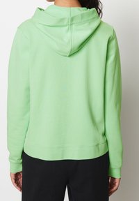 Vihreä puuvillainen huppari, jossa on kiristysnauhallinen huppu. Rentoa istuvuutta ja resorireunukset hihoissa. Sileä pinta ja litteät saumat takana.