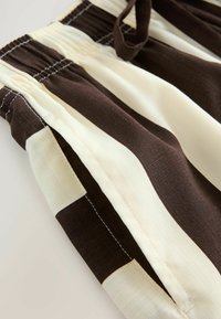 Shorts rayés marron et crème, avec une coupe ample, une taille élastique et des poches latérales avec des détails de couture visibles.