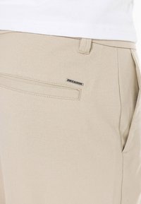 Pantalons beige en tissu mélangé coton, dotés d'une poche arrière avec un contour cousu et d'une petite étiquette logo "PEGA-DOR".