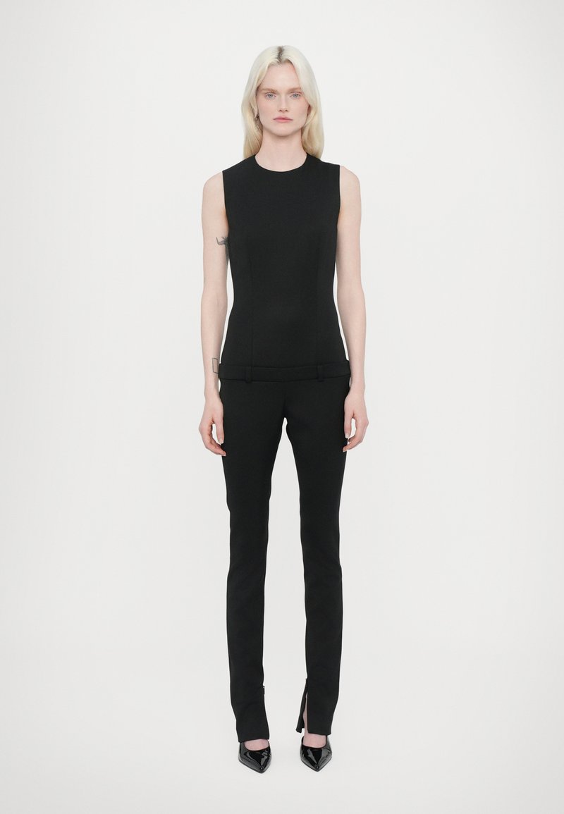 Haut sans manches noir avec une coupe ajustée, associé à un pantalon noir sur mesure avec des fentes latérales et des escarpins en cuir verni à talons aiguilles.