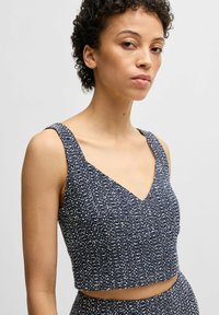 Laivansinis cropped-top V-kaula-aukolla, teksturoitu kudottu kangas, jossa on valkoisia pilkkuja. Paksut olkaimet ja istuva siluetti.