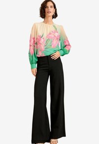 Blusa floreale con design a gradiente rosa e verde, tessuto trasparente e maniche lunghe. Abbinata a pantaloni larghi neri a vita alta.