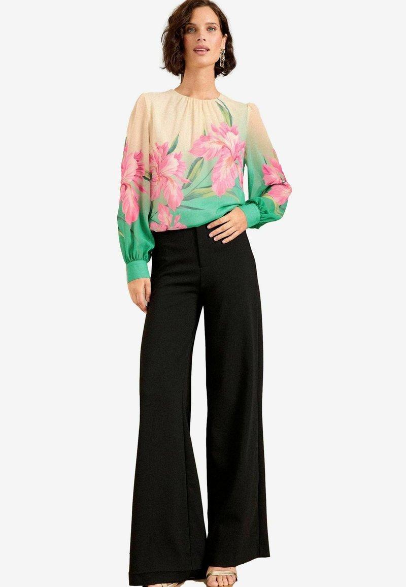 Blusa floreale con design a gradiente rosa e verde, tessuto trasparente e maniche lunghe. Abbinata a pantaloni larghi neri a vita alta.