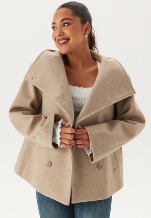 Beige ullblandad kappa med bred krage, dubbelknappning och sänkta axlar. Strukturerad tyg och avslappnad passform med sidfickor.