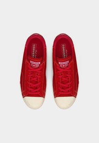 Ζευγάρι κόκκινων χαμηλών Converse All Star αθλητικών παπουτσιών με λευκές λαστιχένιες μύτες και κόκκινα κορδόνια, σε θέα από πάνω, σε λευκό φόντο.