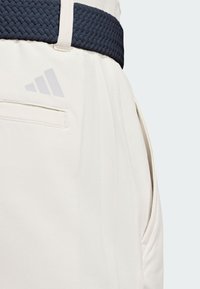 Light beige shorts with a textured navy woven belt. Features a side pocket and includes a subtle grey logo detail on the back.