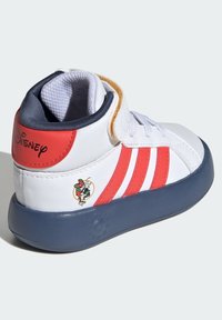 Sneaker bianco alto con strisce rosse e suola blu. Presenta il logo Disney e una grafica del personaggio. Realizzato in materiale sintetico, con colletto imbottito.