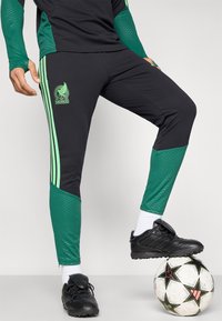 Black athletic pants with green accents and stripes, featuring a Mexico logo. The fabric is smooth with a fitted design, ideal for sports.