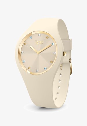 Orologio in silicone beige con una lunetta dorata, dotato di un quadrante off-white testurizzato e dodici indici di ora in cristallo. Lancette e corona dorate.