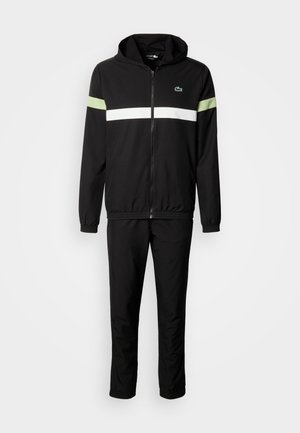 Schwarzer Trainingsanzug mit Reißverschlussjacke, die weiße und hellgrüne Streifen auf den Schultern aufweist. Weicher Stoff, mit Kapuze und elastischen Bündchen.