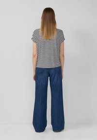 Gestreiftes kurzärmliges Oberteil in Marineblau und Weiß, kombiniert mit weit geschnittenen blauen Jeans aus Denim. Das Outfit zeichnet sich durch eine lässige Passform und ein leichtes Material aus.