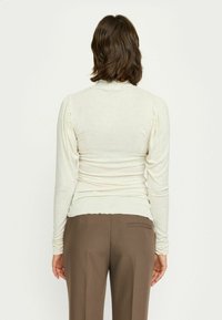 Bluză crem cu mânecă lungă, cu un croi ajustat, detalii cu umeri pliați și țesătură ușoară, asortată cu pantaloni negri eleganți.