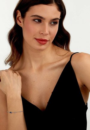 Silberarmband mit blauen Akzenten, zartes Kettendesign, an einem nackten Handgelenk getragen; Model trägt ein ärmelloses schwarzes Oberteil, glatte Haut, subtile Details.