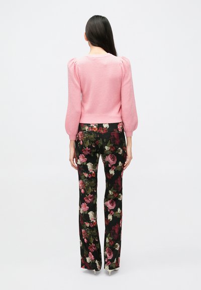 Rozā adīts džemperis ar pūkainām piedurknēm, kopā ar melnām ziedu biksēm ar rozā, zaļām un baltām ziedu nokrāsām.