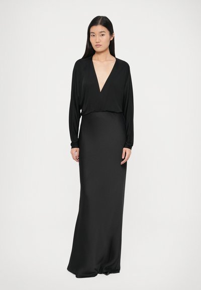 Melna maksi kleita ar dziļu V veida izgriezumu, garām piedurknēm un pieguļošu korseti. Gluda, spīdīga auduma ar elegantu siluetu. Nav redzamu rakstu.