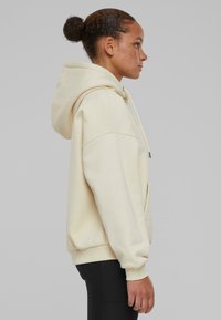 Felpa beige con cappuccio regolabile, tasca a marsupio e polsini a costine. Tessuto morbido, vestibilità comoda e design minimalista.