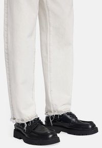 Scarpe di pelle nera con suole spesse, abbinate a jeans bianchi sfilacciati. Le scarpe presentano lacci e una finitura liscia.