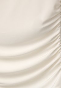 Tessuto bianco con una texture liscia e dettagli arricciati. Il materiale appare leggermente lucido e viene drappeggiato per creare curve morbide.
