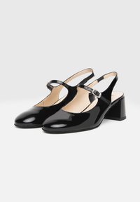 Chaussures slingback en cuir verni noir avec un bout arrondi, un petit talon bloc, et une bride ajustable à la cheville. Texture lisse et brillante.