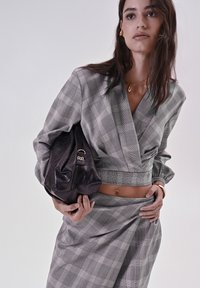 Cropped top e gonna a quadri grigi con maniche voluminose, abbinati a una borsa nera lucida con accessori dorati.