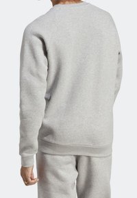 Man med ljusgrå sweatshirt och matchande sweatpants, visad från ryggen med vänster hand synlig och en guldring på fingret.