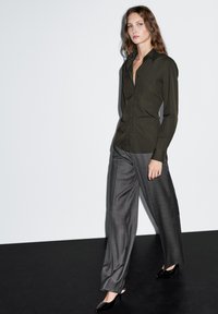 Dark olive green button-up shirt with a pointed collar, paired with grey wide-leg trousers and black pointed-toe heels. Smooth textures.