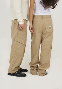 Beige cargobroeken van een katoenmix, met meerdere zakken en een losse pasvorm. Etiket op de rechter achterzak. Zwarte schoenen gedragen.