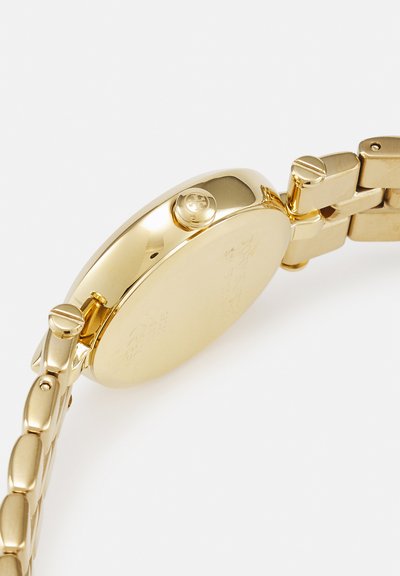 Orologio da polso in metallo dorato con vista laterale, pulsanti corona e bracciale collegato su sfondo bianco semplice.