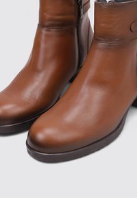 Botas de cuero marrón hasta el tobillo con un acabado suave, punteras redondeadas y cremalleras laterales. Tienen una suela robusta con un ligero tacón para mayor comodidad.