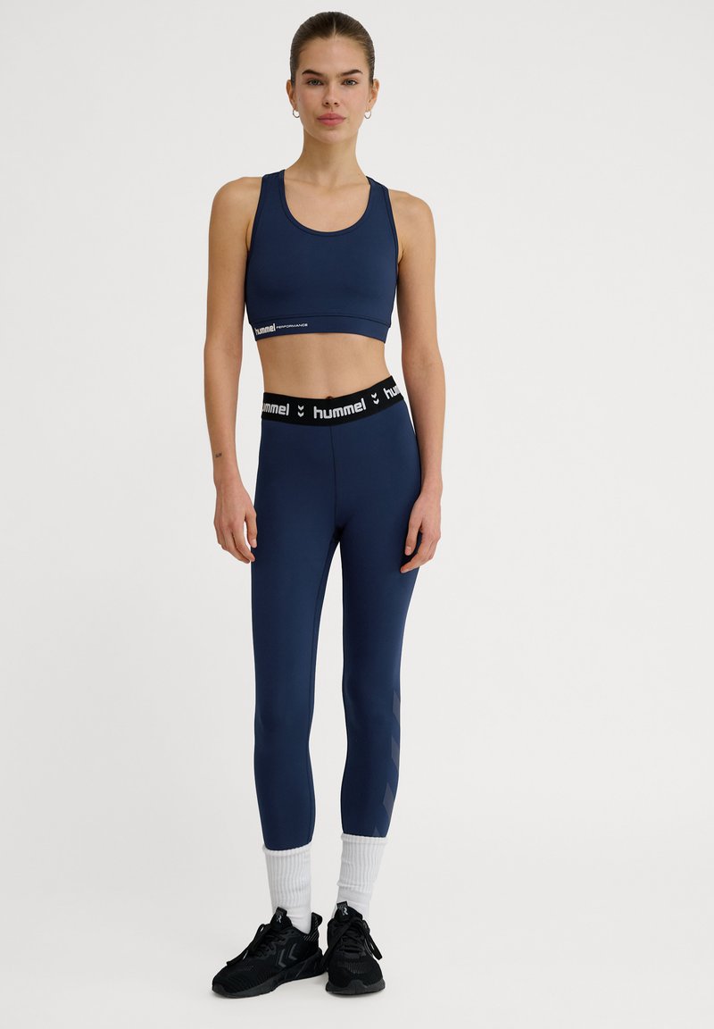 Marinblå sport-bh och tights med en svart midja med en logotyp. Tightsen har ett subtilt mönster på sidan och är figurnära.