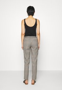 Černý top bez rukávů spárovaný s kalhotami s vysokým pasem v károvém vzoru, který kombinuje světle béžovou a černou barvu. Úzký střih, délka ke kotníkům.